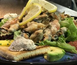Meeresfrüchtesalat mit Zitronenscheiben, Toast, Avocado und einem Klecks Creme auf einem blauen Teller.