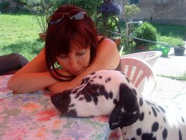 Frau lehnt sich auf einen Tisch im Garten, ein Dalmatiner liegt neben ihr.