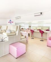 Sala de spa infantil con sillones beige, taburetes rosas y espejos iluminados.