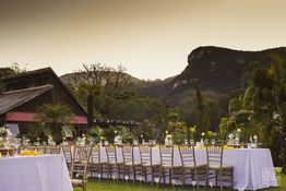 Mesa de jantar ao ar livre decorada, com montanhas e vegetação ao fundo.