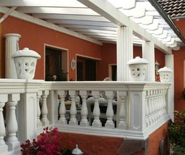 Weiße Balustrade mit Säulen und Blumentopf auf einer Terrasse, umgeben von roten Wänden.