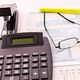 Calculator, documents, glasses, and stapler on a desk, representing office or tax work.