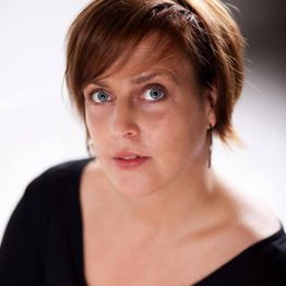 Eine Frau mit kurzen braunen Haaren, blauem Blick und schwarzem Oberteil schaut direkt in die Kamera.