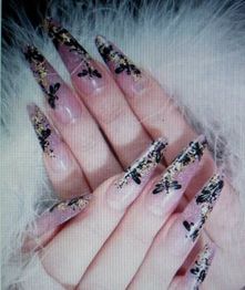 Langgestreckte Fingernägel mit floralem Design und goldenen Akzenten auf weißem Hintergrund.