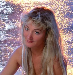 Eine lächelnde Frau mit langen blonden Haaren vor einem funkelnden Hintergrund.