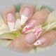 Nahaufnahme von Fingernägeln mit French Maniküre und Blumenmuster auf einer Blüte.