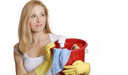 Frau mit gelbem Handschuh hält roten Eimer voller Reinigungsutensilien.