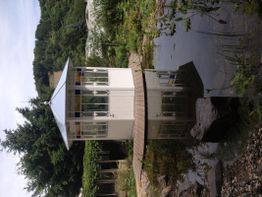 Weißer Pavillon mit Spiegelung in einem Teich, umgeben von Bäumen und Pflanzen.