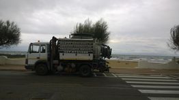 Camion per la raccolta rifiuti parcheggiato vicino alla spiaggia, cielo nuvoloso sullo sfondo.