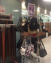 Laden mit Taschen und Gürtel auf Ständern, Preisangaben sichtbar, Fliesenboden.