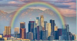 City skyline with a rainbow arching over tall buildings and mountains in the background.