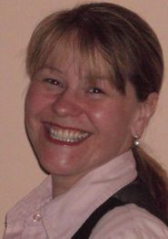 Eine Frau mit Pferdeschwanz lächelt breit in die Kamera und trägt ein Hemd mit Weste.