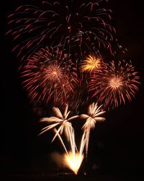 Feuerwerk explodiert am Nachthimmel mit leuchtenden Farben und Palmenformen.