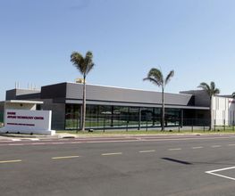 Centro tecnológico moderno com fachada de vidro, cercado por palmeiras à beira de uma estrada asfaltada.