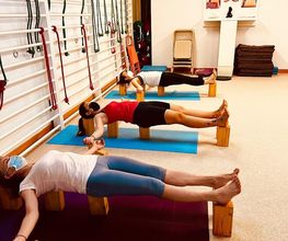 Personas haciendo yoga en un estudio con bloques de madera y equipos en la pared.