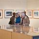 People viewing framed photographs in an art gallery, examining details and discussing.