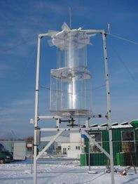 Windturbine im Schnee, umgeben von Gebäuden und klarem Himmel.