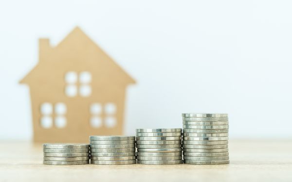 Hinter vier aufgereihten Stapeln von Geldmünzen steht ein Modell eines Hauses aus Holz. Das symbolisiert den Vorteil von Abschreibungen auf Immobilien.