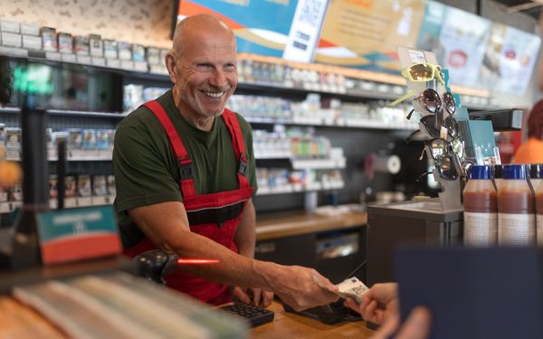 Tankstellen-Mitarbeiter verkauft etwas in Tankstellen-Shop