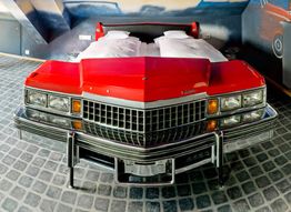 Bett mit rotem Auto-Design wie ein Oldtimer in einem Zimmer mit gepflastertem Boden und Wandmalereien.