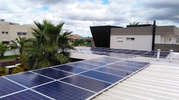 Painéis solares em telhado de casa, céu parcialmente nublado ao fundo.