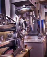 Alte Industriemaschinen in einer Werkstatt mit blauer und grauer Einrichtung und einem Fenster links.