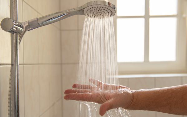 Es wird eine Hand unter das laufende Wasser eines Duschkopfs gehalten.