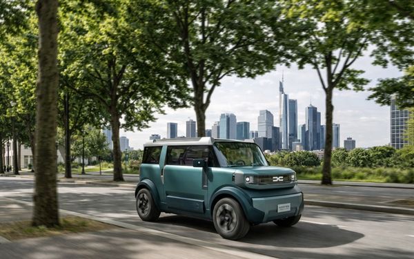 Ein grüner Dacia Hipster fährt durch eine Allee, im Hintergrund ist die Skyline einer Großstadt zu erkennen.