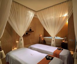 Sala de spa con dos camas, cortinas blancas y una bañera al fondo.