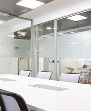 Sala de reuniones moderna con mesa blanca y sillas negras, paredes de vidrio y luz natural.