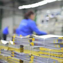 Worker in blue uniform stacking yellow-paged books in a warehouse.