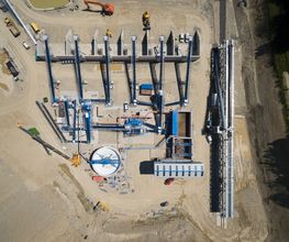 Luftaufnahme einer Baustelle mit Maschinen, Kränen und Gebäudestrukturen.