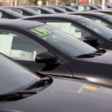 Row of black cars for sale with price tags displayed on windshields.