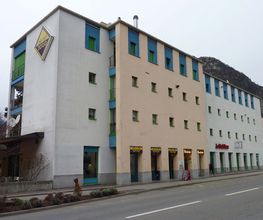 Mehrfarbiges Gebäude mit Schildern und Fenstern an einer Straße, Berge im Hintergrund.