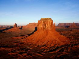 Rote Felsformationen im Monument Valley bei klarem Himmel und Sonnenschein.