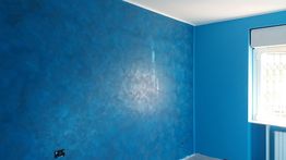 Parete di una stanza dipinta di blu con una finestra sulla destra e luce naturale.