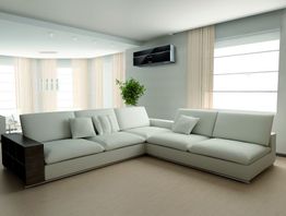 Sala moderna com sofá em L branco, ar-condicionado e planta ao fundo.