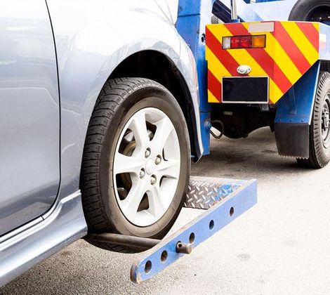 Auto blu chiaro sollevata da un carro attrezzi su una strada asfaltata.