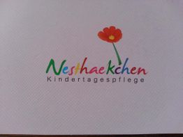 Buntes Logo der "Nesthaekchen Kindertagespflege" mit einer roten Blume darüber.