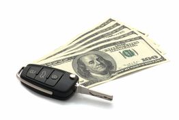 Car key beside fanned out $100 bills on a white background.