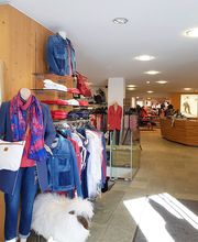 Modegeschäft mit Schaufensterpuppe in Jeans und Schal, Klamottenregale und Holzverkleidung.