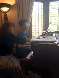 A boy and a woman at a piano, with the woman pointing at sheet music.
