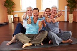 Gruppentraining: Vier Frauen sitzen auf Yogamatten, lachen und zeigen Daumen hoch.