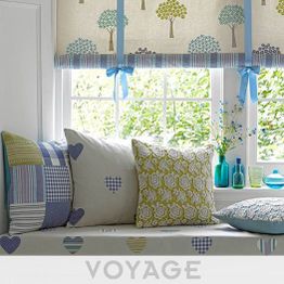 Finestra con tende decorate, cuscini a motivi e vasi colorati su un davanzale imbottito.