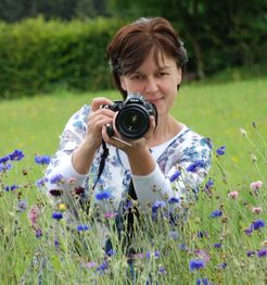 Frau in Blumenwiese mit Kamera, bereit zum Fotografieren.