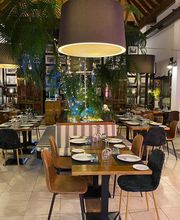 Restaurante elegante con mesas dispuestas, lámparas colgantes y decoración de plantas.