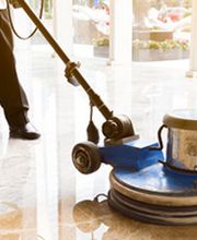 Person poliert glänzenden Marmorboden mit einer Reinigungsmaschine in einem sonnigen Raum.