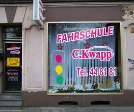 Fahrschule C. Kwapp mit Telefonnummer auf Schaufenster und Ampelsymbolen an einer Straßenfront.