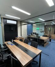 Escritório moderno com mesas de madeira, cadeiras pretas e divisórias de vidro.