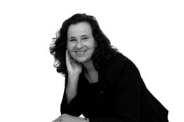 Schwarz-weiß Porträt: Frau lächelt in die Kamera, eine Hand am Kinn, im Blazer.